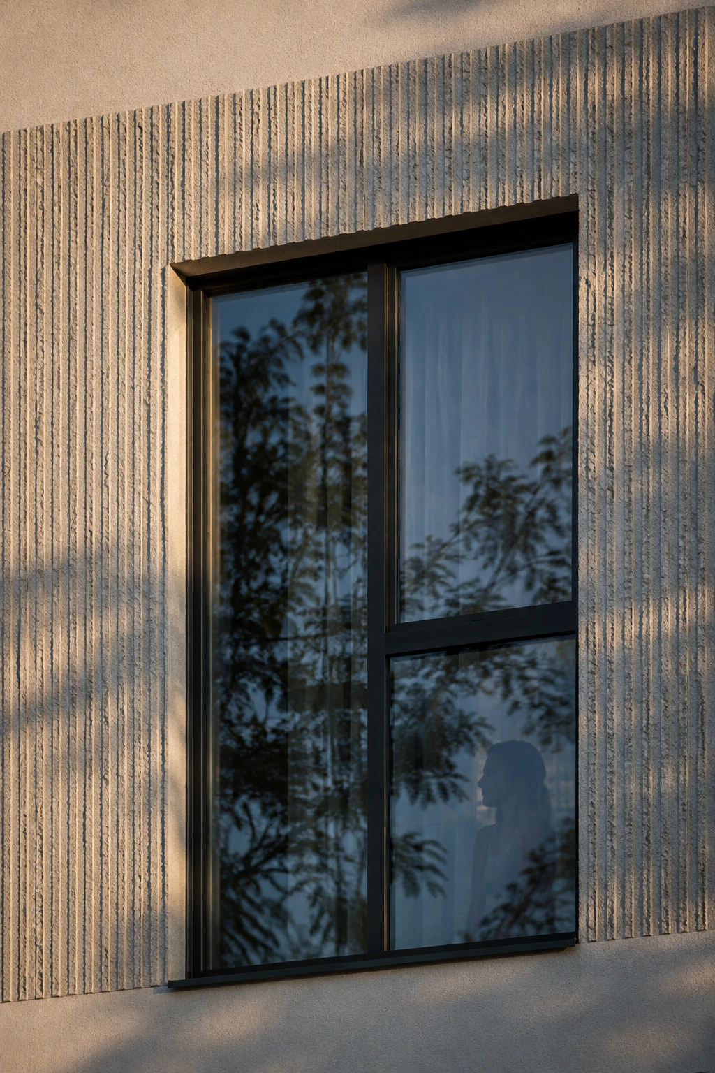 Fenster in der strukturierten Fassade, in dem sich Bäume spiegeln